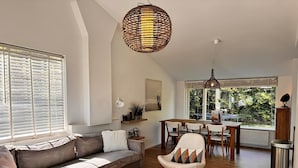 A modern living room with a sofa, a round table, and chairs. There is a window with blinds, a hanging light fixture, and a radiator.