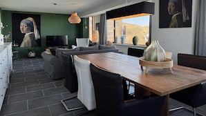 A modern living room with a large painting, a dining area with a wooden table, and a view of the desert through the window. - Callantsoger Staete A210 (Callantsoog)