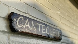 A weathered metal sign with the word "CANTECLER" mounted on a white brick wall.