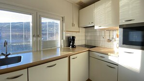 A modern kitchen with white cabinets, a stainless steel sink, and a large window with blinds.