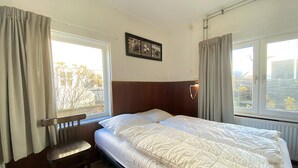 A hotel room with a bed, a chair, and two windows with curtains.