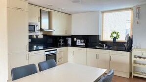 A modern kitchen with white cabinets, a black countertop, and a dining area with a table and chairs. - Callantsoger Staete A306 (Callantsoog)