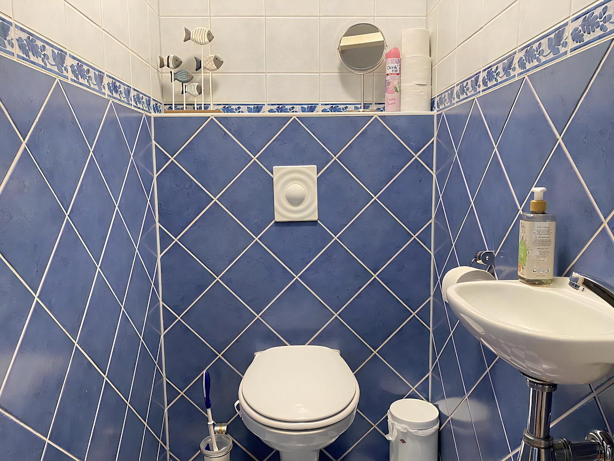 A bathroom with blue tiled walls, a white toilet, a sink, and a hand dryer.