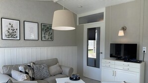 A modern living room with a sofa, armchairs, a coffee table, and a TV. There are framed artworks on the wall and a window with a view. - 3 bedroom accommodation in Callantsoog (Callantsoog)
