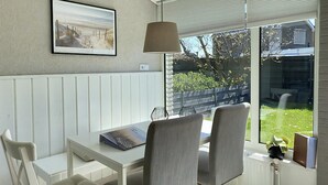 A sunlit room with a table, chairs, a framed picture, and a window overlooking a garden. - 3 bedroom accommodation in Callantsoog (Callantsoog)