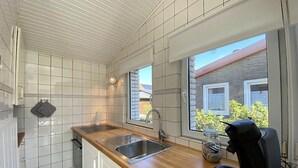 A modern kitchen with white tiles, a wooden countertop, a built-in sink, and a window with a view of a brick building and greenery. - 3 bedroom accommodation in Callantsoog (Callantsoog)