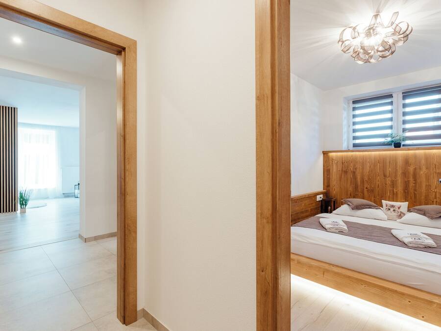 Un dormitorio con cabecera de madera, una cama con almohadas, una mesita de noche y una ventana con persianas.