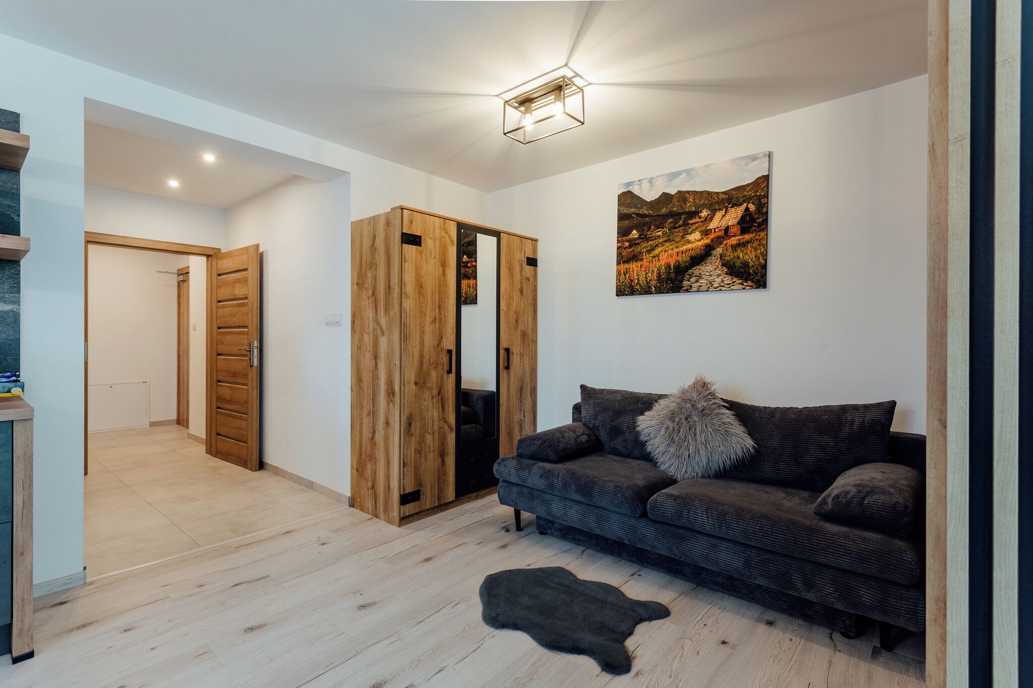 Una sala de estar moderna con un sofá gris oscuro, un armario de madera y un cuadro de un paisaje montañoso.