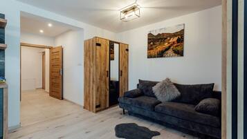 Una sala de estar moderna con un sofá gris oscuro, un armario de madera y un cuadro de un paisaje montañoso.
