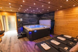Um espaço de spa com banheira de hidromassagem, mesas de massagem, paredes de madeira e um painel de parede de pedra.