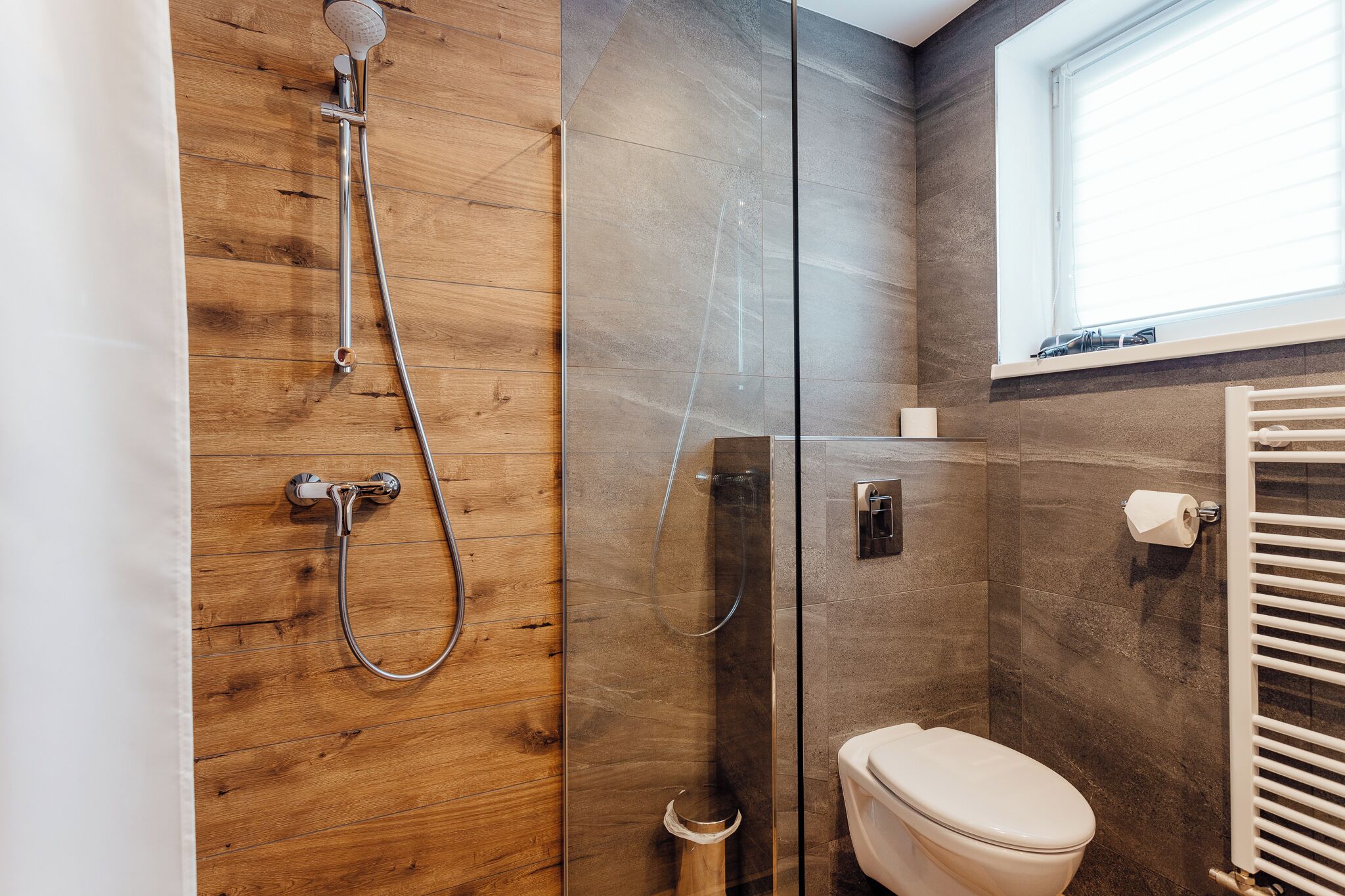 A modern bathroom with a wooden shower enclosure, a glass shower stall, and a toilet.