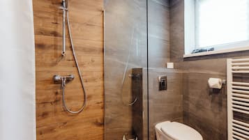 A modern bathroom with a wooden shower enclosure, a glass shower stall, and a toilet.