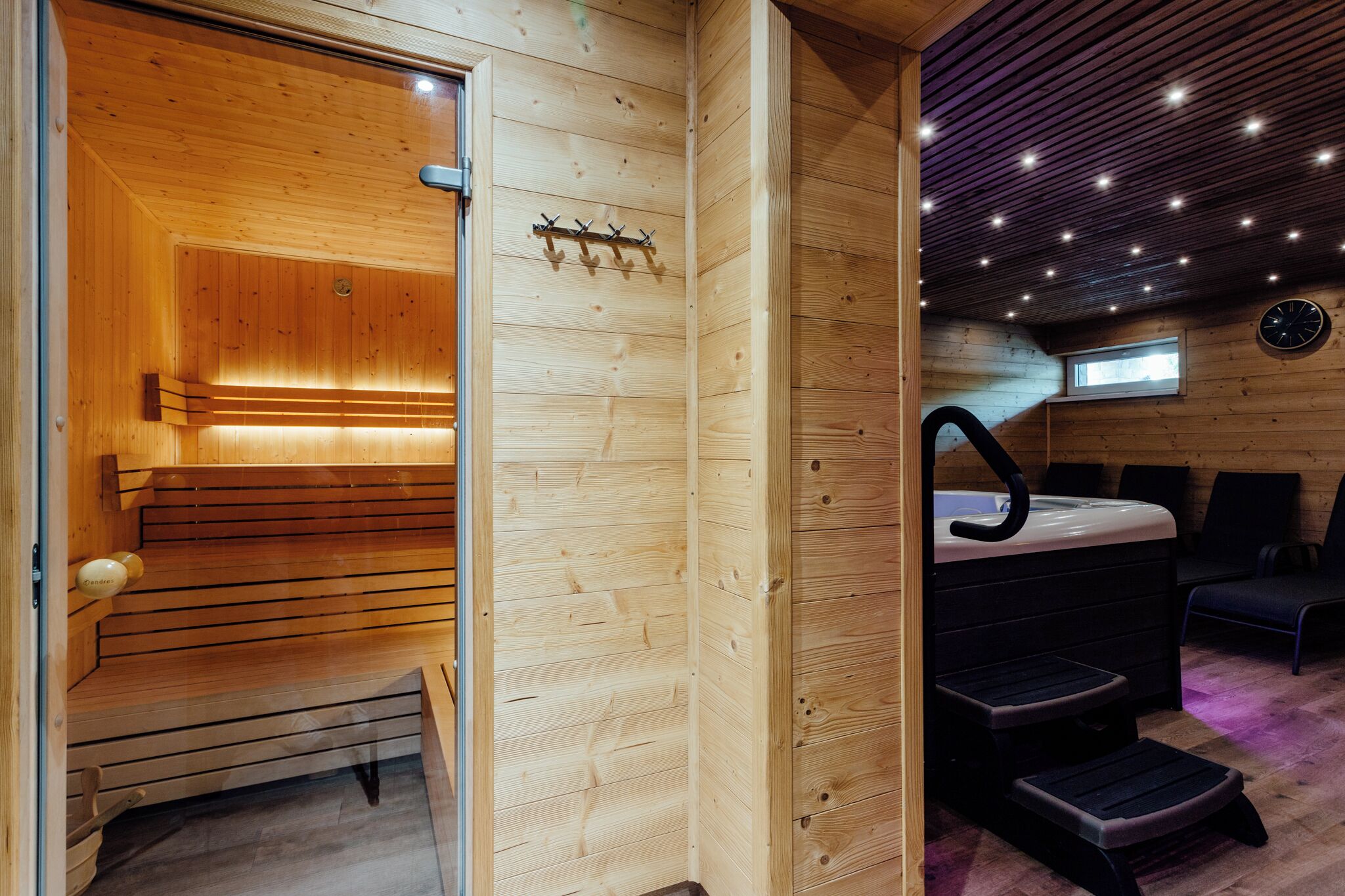 A wooden sauna room with benches and a bench seat, a wooden wall with a coat rack, and a window.