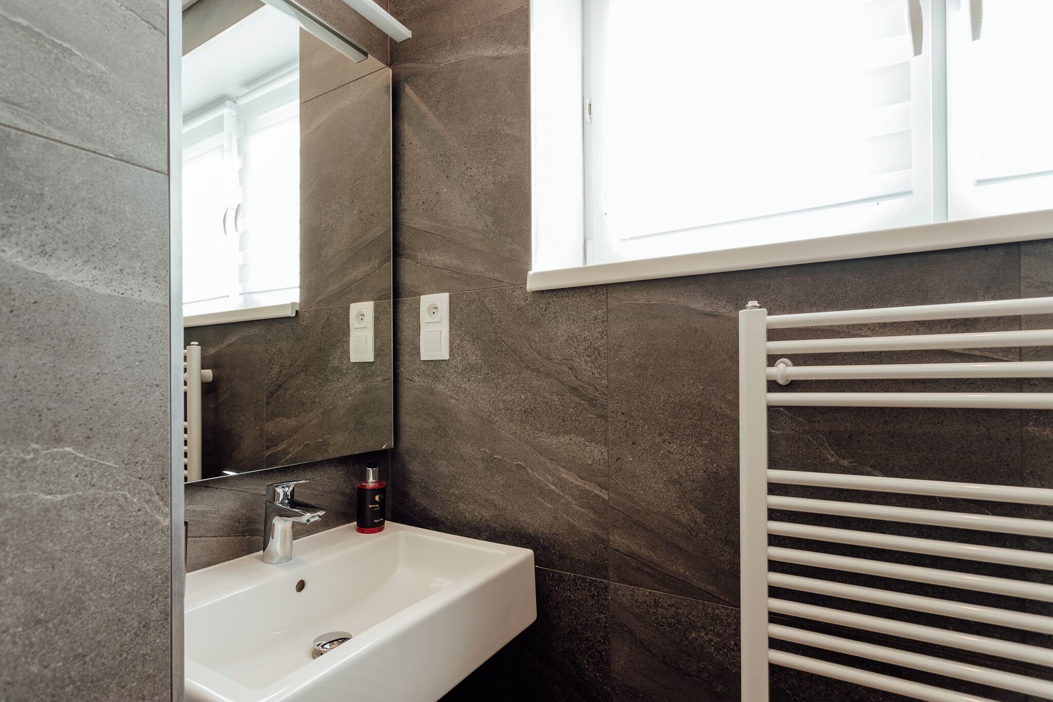 A modern bathroom with a white sink, a mirror, and a towel rack.