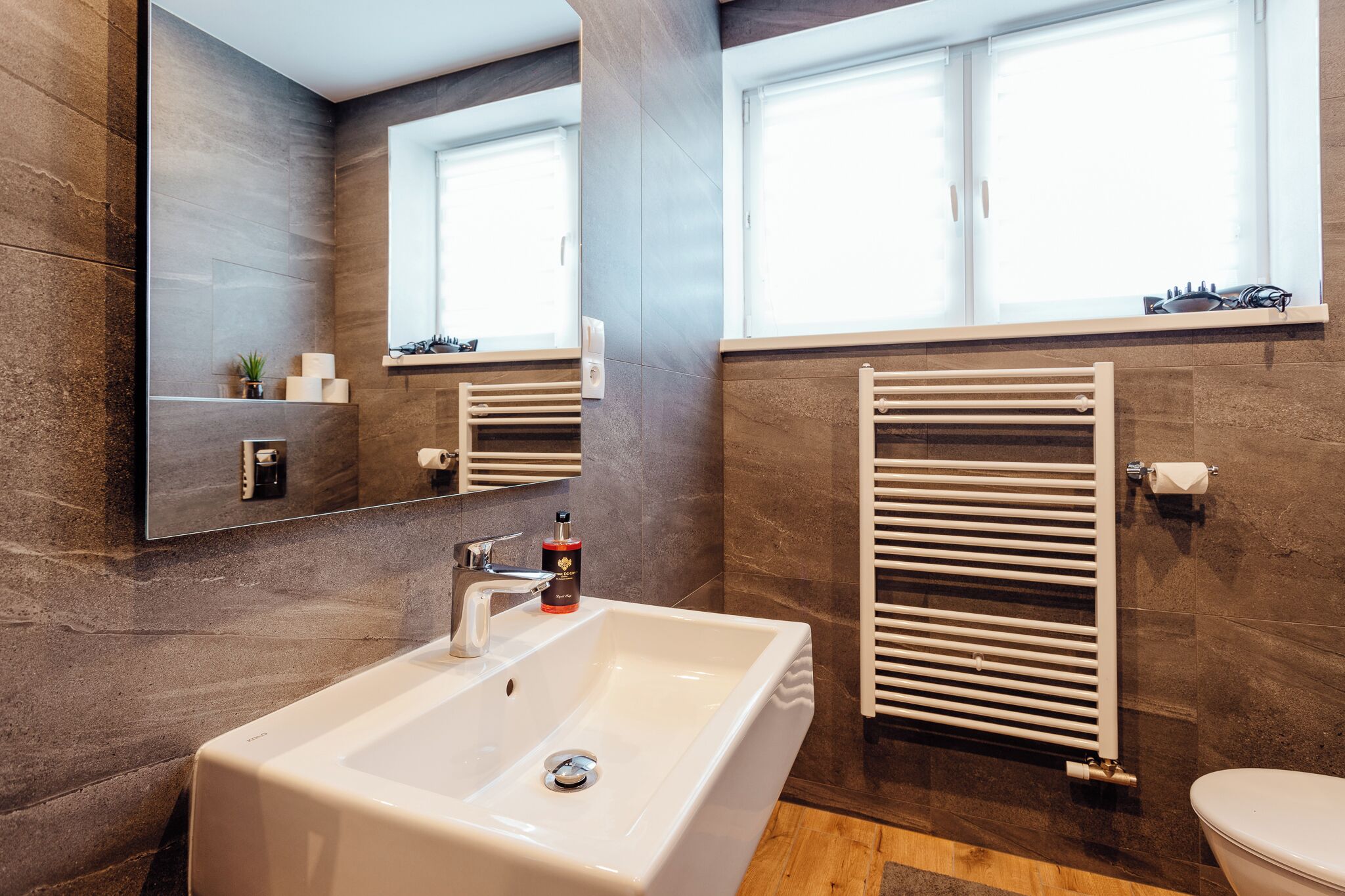 A modern bathroom with a large mirror, a white sink, a towel rack, and a toilet.