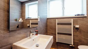 A modern bathroom with a large mirror, a white sink, a towel rack, and a toilet.