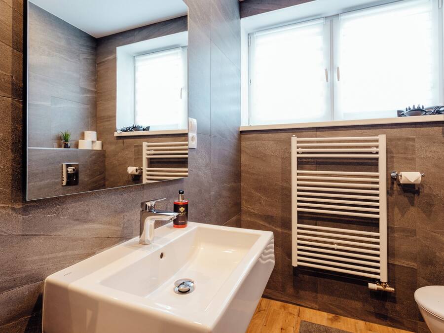A modern bathroom with a large mirror, a white sink, a towel rack, and a toilet.