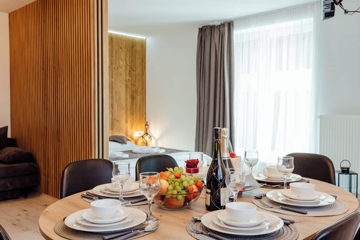 A dining area with a round table set for four, a fruit bowl, wine glasses, and a bottle of wine.