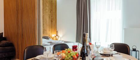 A dining area with a round table set for four, a fruit bowl, wine glasses, and a bottle of wine.