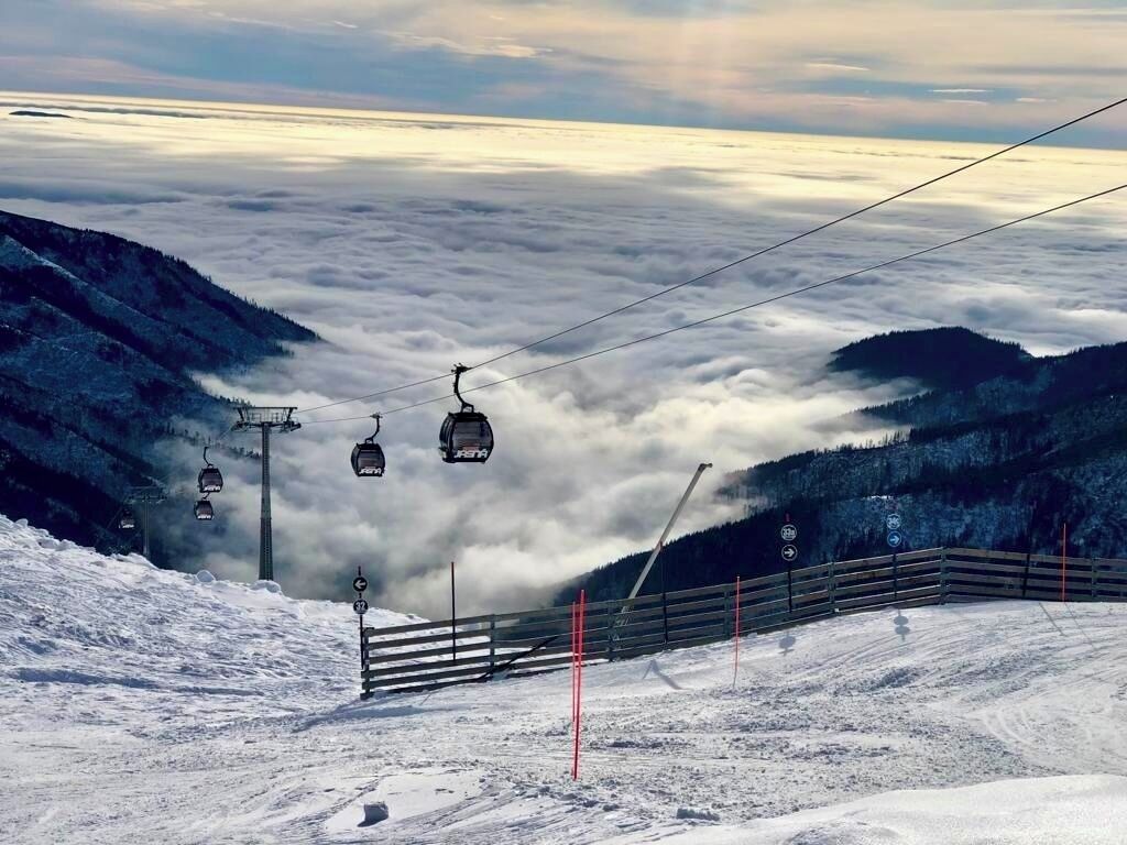 Un télésiège qui traverse une montagne enneigée, avec une vallée boisée en contrebas.