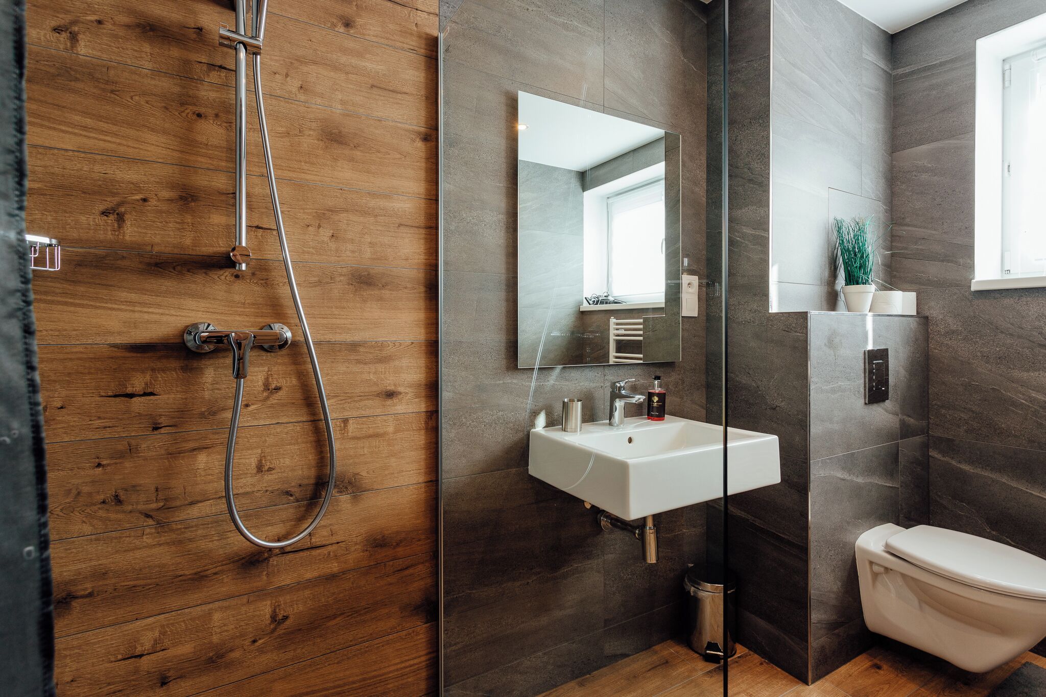 A modern bathroom with a wooden shower enclosure, a white sink, a mirror, and a toilet.
