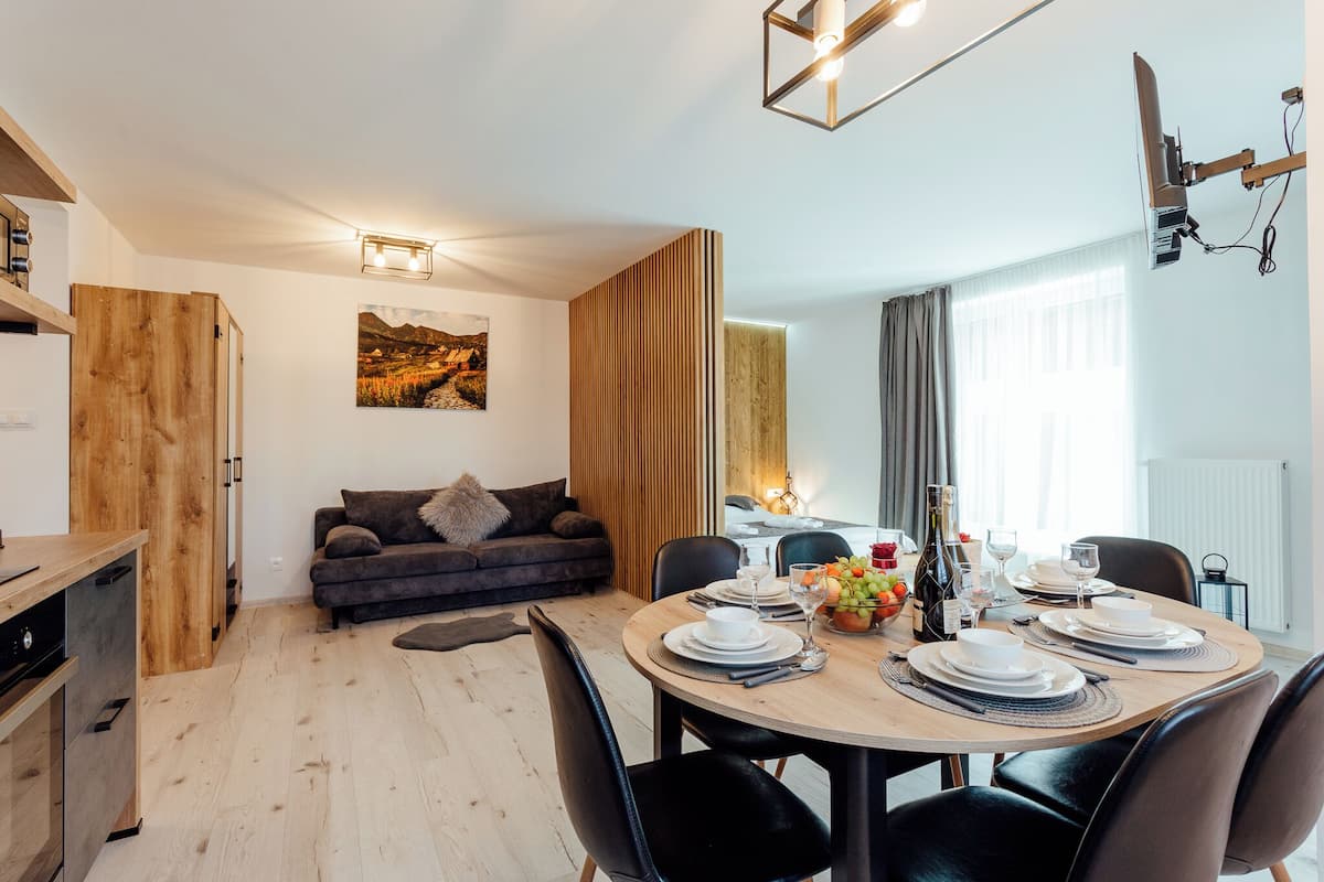 A modern living room with a dining area, wooden furniture, a sofa, and a painting on the wall.