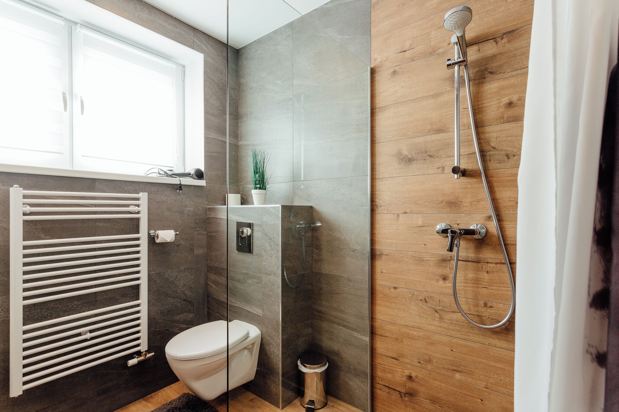 Un baño moderno con cabina de ducha de vidrio, inodoro blanco y suelo de madera.