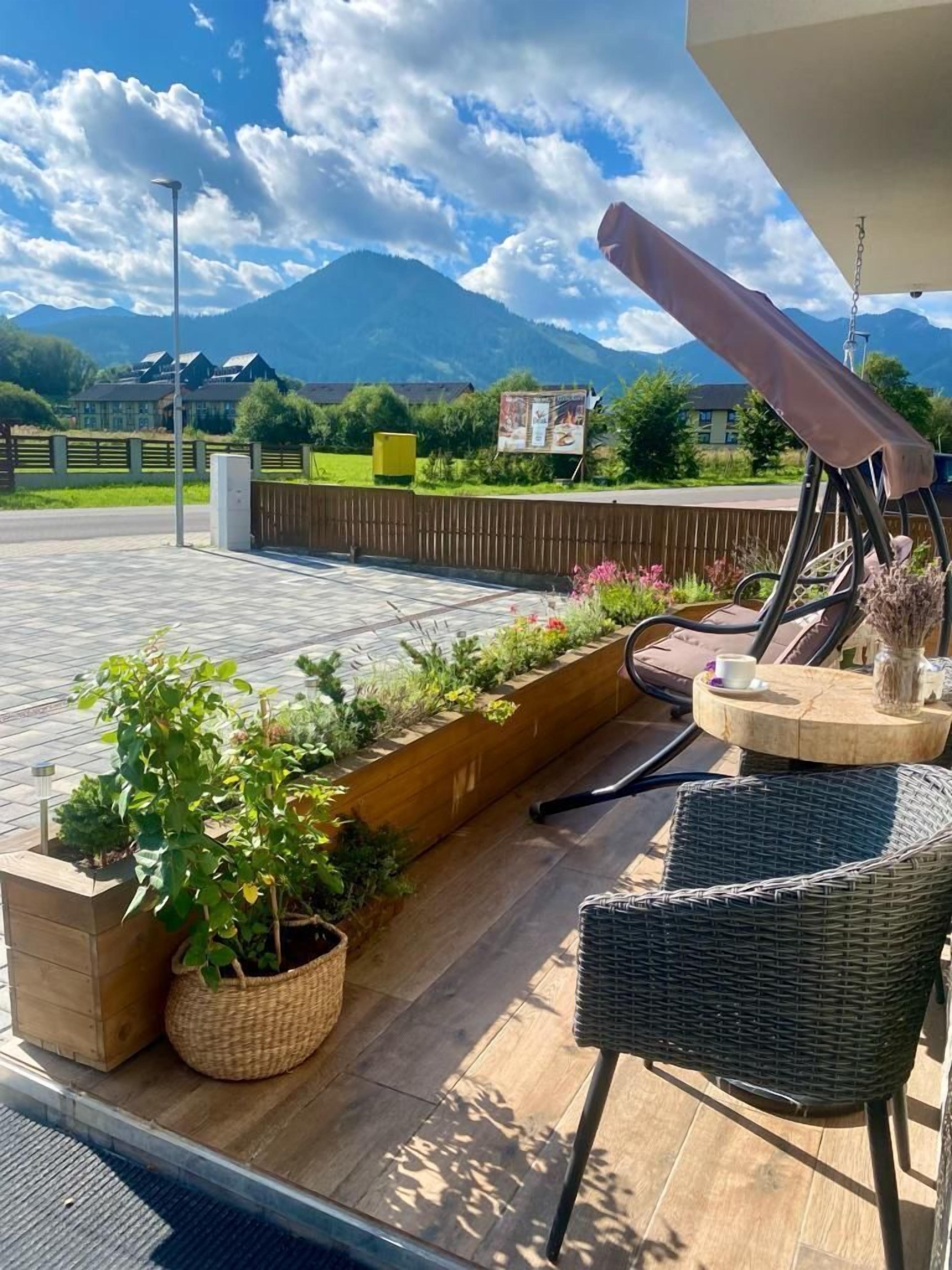 A patio area with wicker furniture, a wooden planter with plants, and a view of mountains.