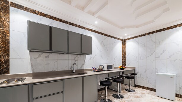 A modern kitchen with marble tiles, a built-in microwave, a refrigerator, and a bar area with stools. - Al Qasr Hotel Suites -Al Tahlia District (Khamis Mushait)