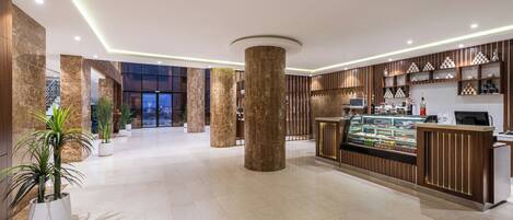 A spacious lobby with marble columns, a reception area with a display case, and potted plants.