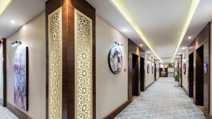 A hotel corridor with a patterned carpet, decorative panels, and framed artwork on the walls. - Al Qasr Hotel Suites -Al Tahlia District (Khamis Mushait)