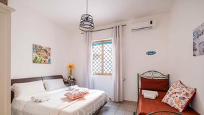 A bedroom with a bed, a nightstand, a window with curtains, and an air conditioning unit. - Sunny Haven Villa In Torre Lapillo (Porto Cesareo)