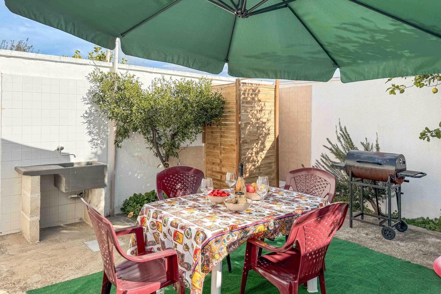 A patio with a table set for dining, surrounded by chairs, a grill, and a sink.