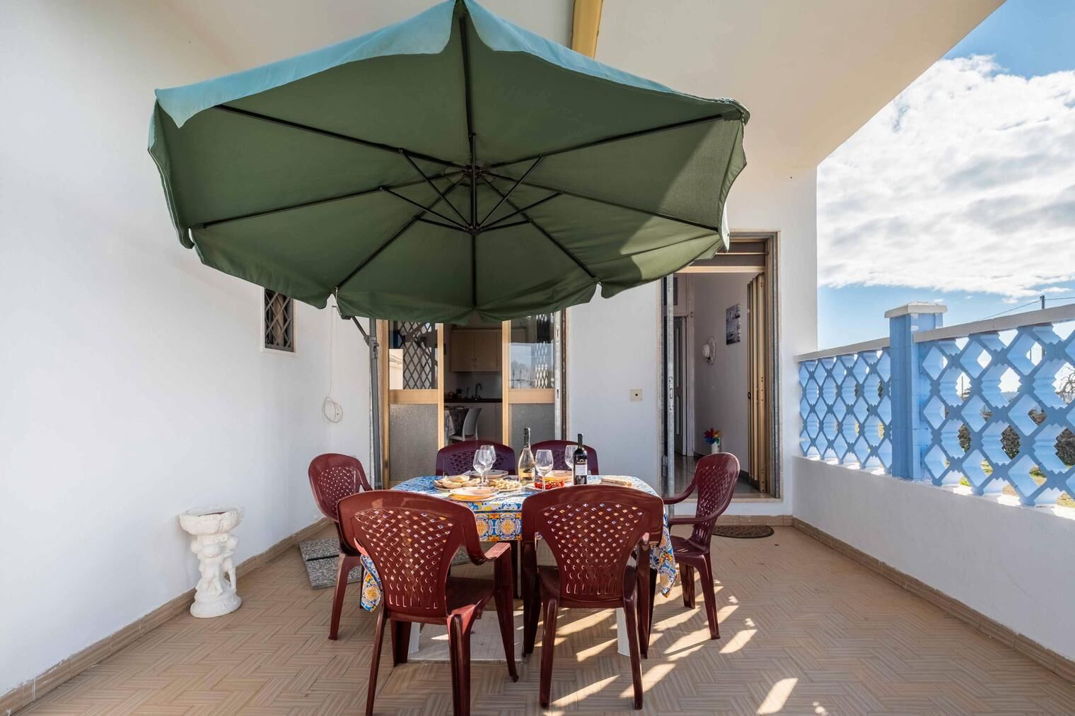 A dining area with a table set for four, a green umbrella, and a view of the sea.