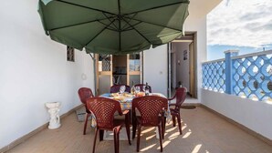 A dining area with a table set for four, a green umbrella, and a view of the sea. - Sunny Haven Villa In Torre Lapillo (Porto Cesareo)