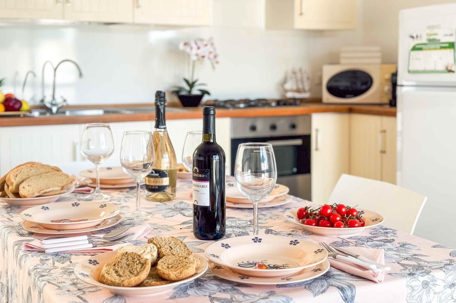 A dining table set with plates, glasses, a bottle of wine, and food.
