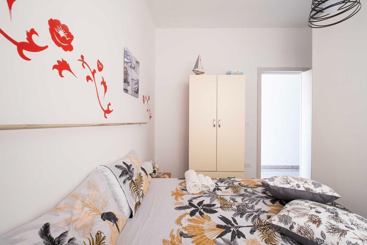 A bedroom with a bed, a wardrobe, and a wall with red floral artwork.
