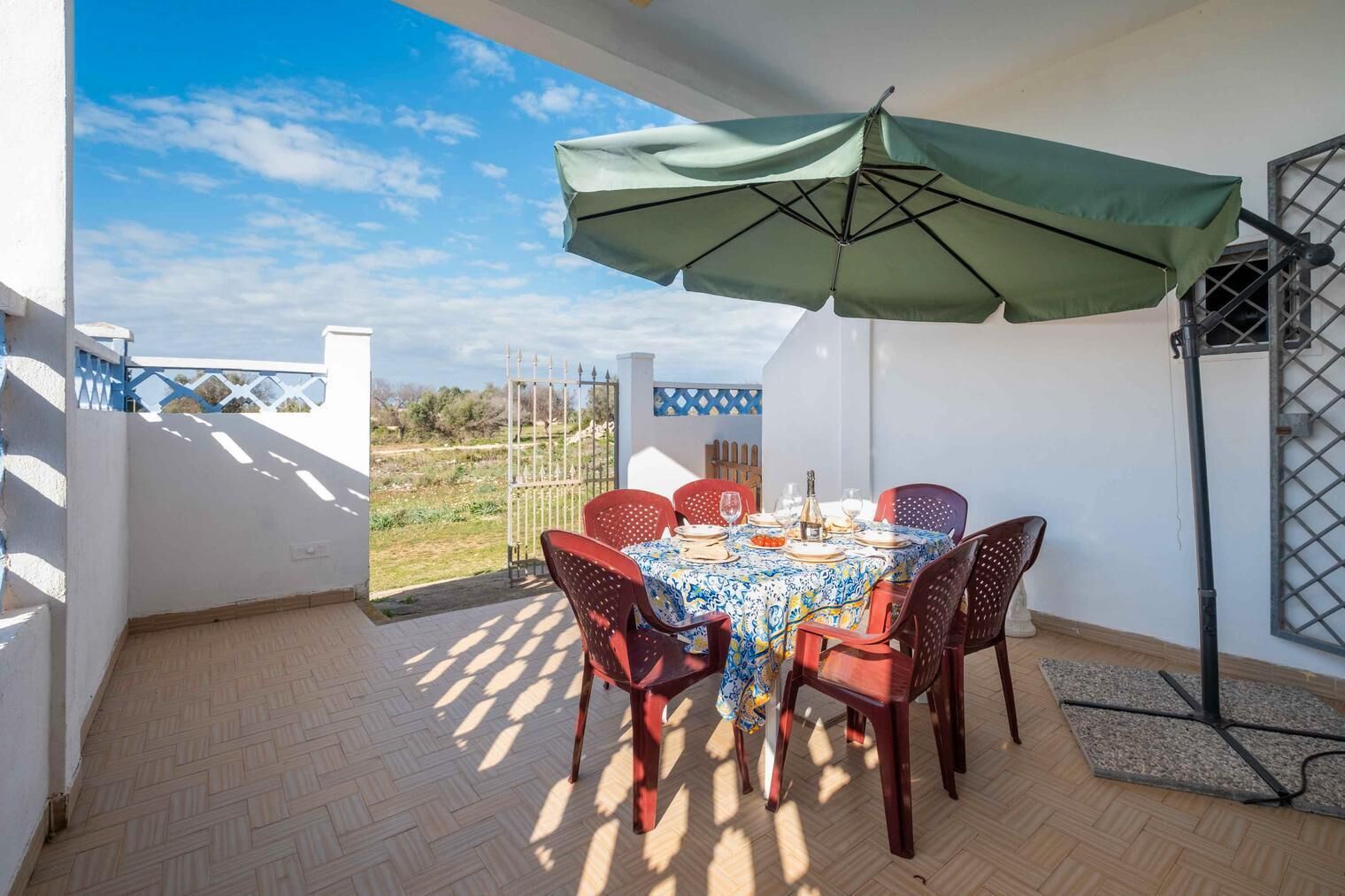 Un patio con una mesa lista para comer, rodeada de sillas, bajo un paraguas grande.