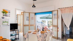 A dining area with a table set for four, a television, and a view of the outside. - Sunny Haven Villa In Torre Lapillo (Porto Cesareo)