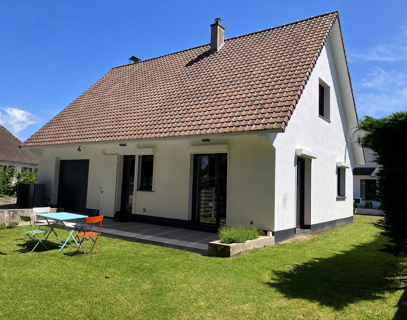 A single-story house with a tiled roof, a front door, and a small patio area with a table and chairs.