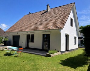 A single-story house with a tiled roof, a front door, and a small patio area with a table and chairs.