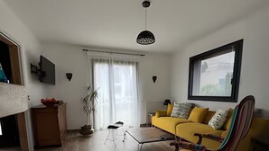 A modern living room with a yellow sofa, a striped armchair, and a coffee table. There is a window with a view of buildings, a potted plant, and a hanging light fixture. - Near Le Touquet, renovated villa for a relaxing break with family or friends. (Cucq)