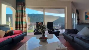 A spacious living room with a large glass door leading to a balcony, a black sofa, a red sofa, and a coffee table with a vase of flowers. - Casa Vale vinagre - Villa large pool for max. 8 persons (São Bartolomeu de Messines)