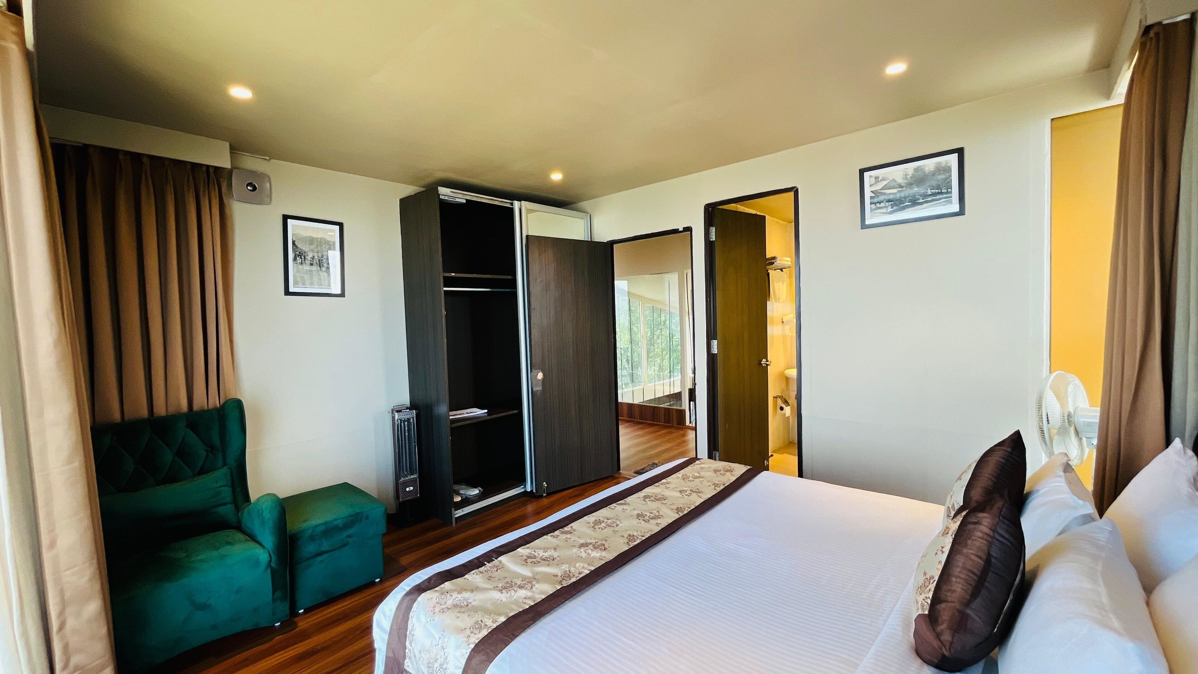 Habitación de hotel con cama, un sillón verde, un armario y un baño visible a través de una puerta abierta.