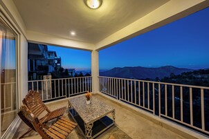 Un balcón con mesa y sillas, barandilla y vistas a las montañas.