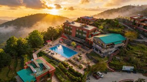 A resort with a swimming pool, multiple buildings, and a mountainous backdrop. - Foxoso Aamari Resort A Luxury Retreat (Kosiyakutoli)