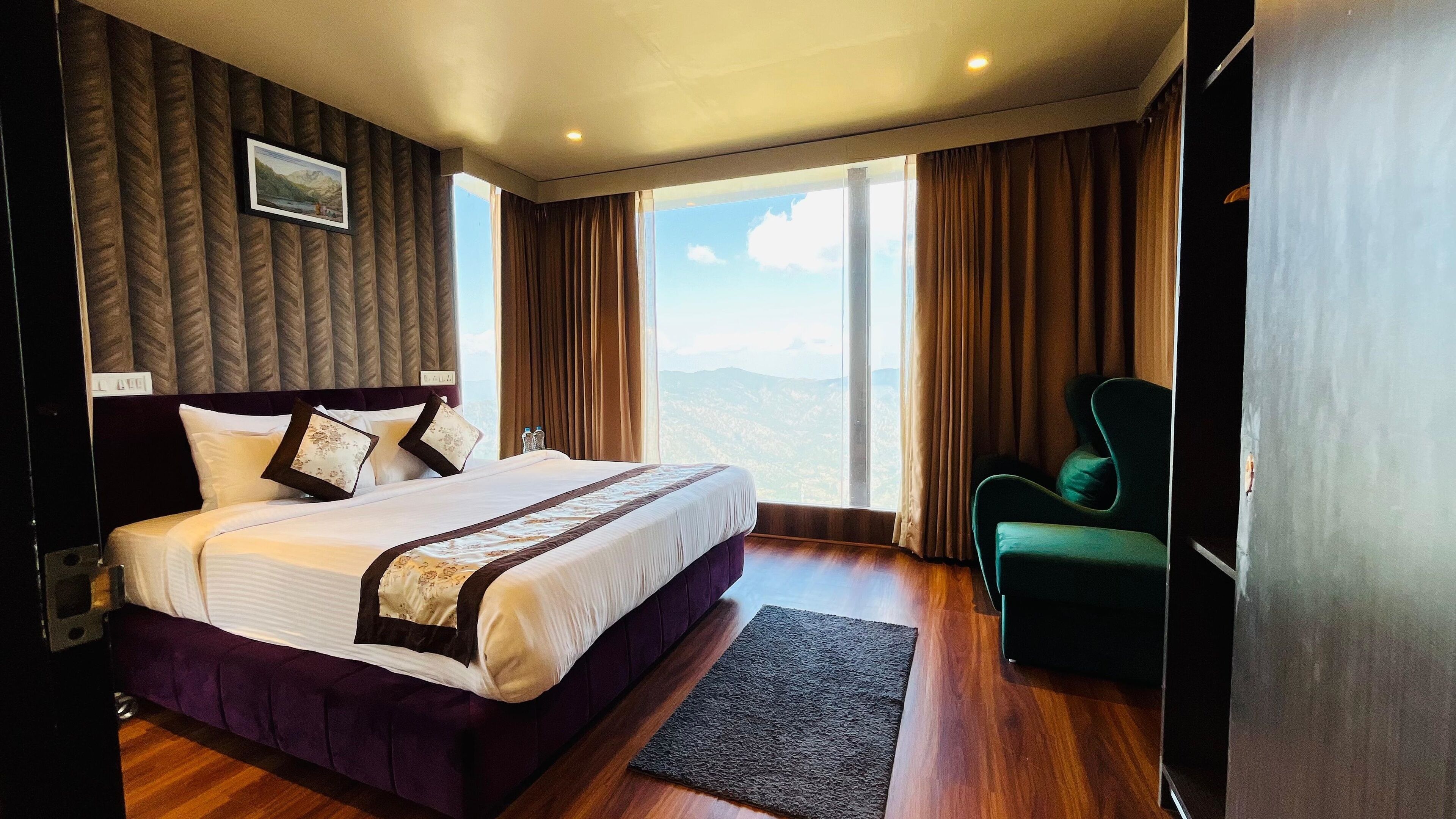 A hotel room with a large bed, a view of the mountains, and a green armchair.