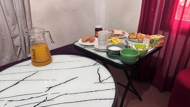 Een ontbijttafel met een glazen karaf, eieren, een pot jam, een mok en een doos cornflakes.