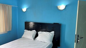 Un letto con una testiera nera e biancheria bianca in una stanza dalle pareti blu e due luci a parete.