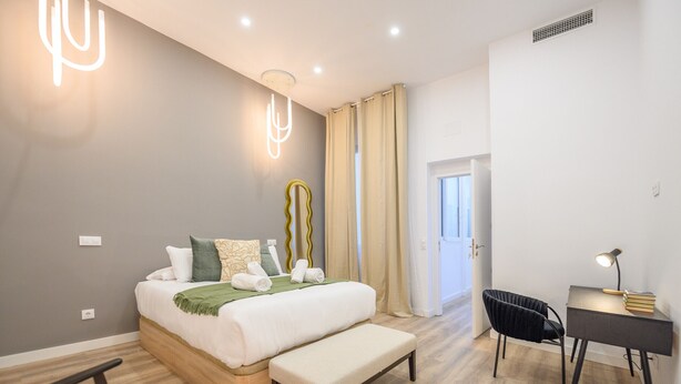 Quarto moderno com cama, banqueta, escrivaninha e cadeira.